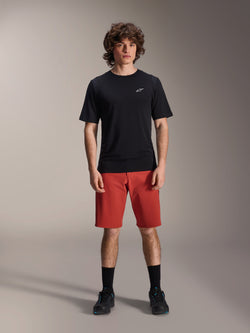 Alpinestars A-Dura Elite Shorts, MTB mountainbike shorts, donkeroranje, gedragen met een zwart shirt met korte mouwen en fietsschoenen, technische fietskleding voor mountainbiken