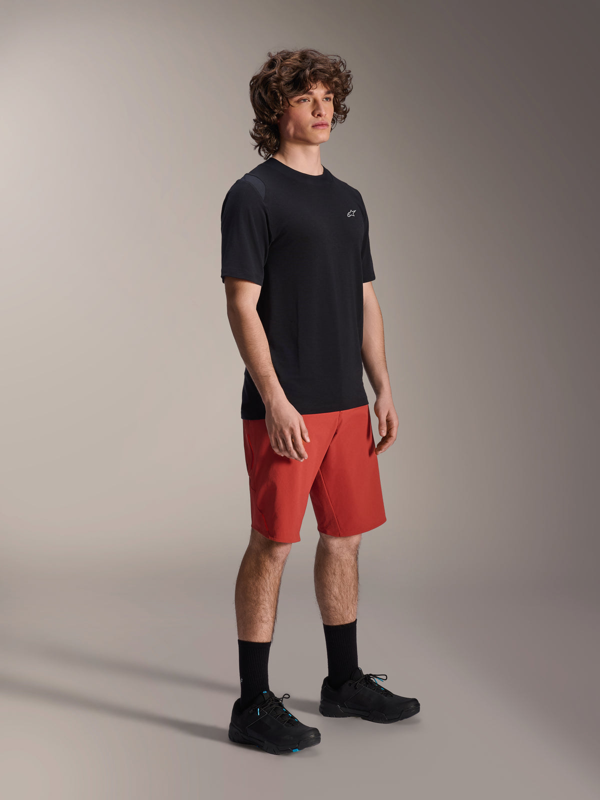 Alpinestars A-Dura Elite Shorts in donkeroranje en A-Dura Dri Wool Jersey met korte mouwen in het zwart, mountainbike-kleding, mannelijk model met zwarte sokken en schoenen, atletisch ontwerp voor off-road fietsen