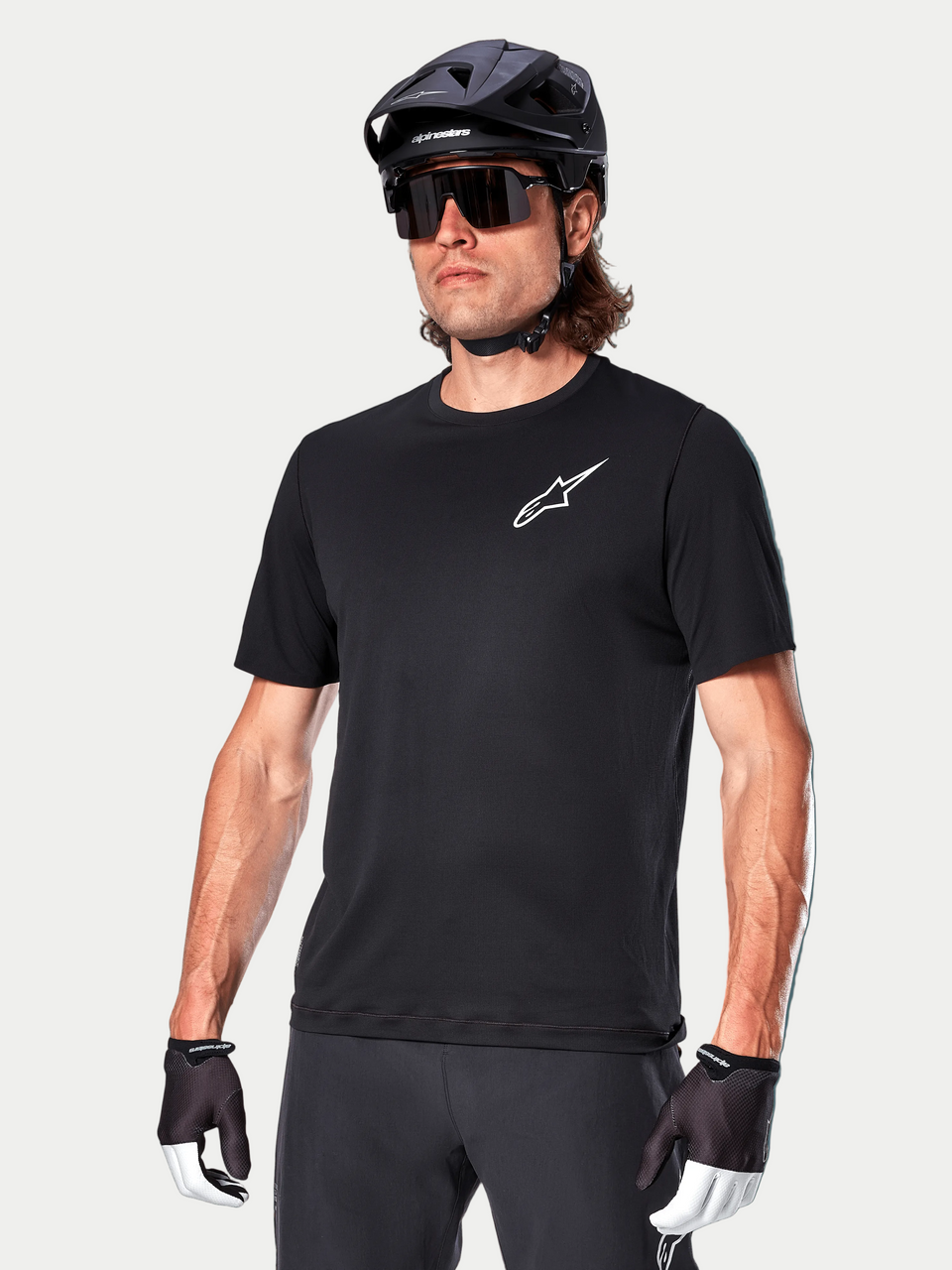Alpinestars A-Aria Astar Short Sleeve Jersey in Black, worn by a cyclist with a black MTB helmet and sunglasses, featuring a white Astar logo on the chest, lightweight and breathable performance gear for trail riding