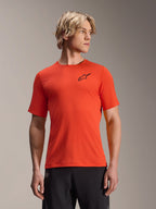 Alpinestars A-Aria Astar Jersey met korte mouwen, Spicy Orange met zwart sterlogo, MTB-mountainbikeshirt voor heren, performance pasvorm, gedragen door een mannelijk model met blond haar en een zwarte broek