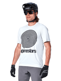 Alpinestars A-Dura Oscar Jersey met korte mouwen, White Dove wit met zwarte heritage spiraalgrafiek en logo, gedragen met zwarte MTB-helm en handschoenen, sportieve performance mountainbikekleding