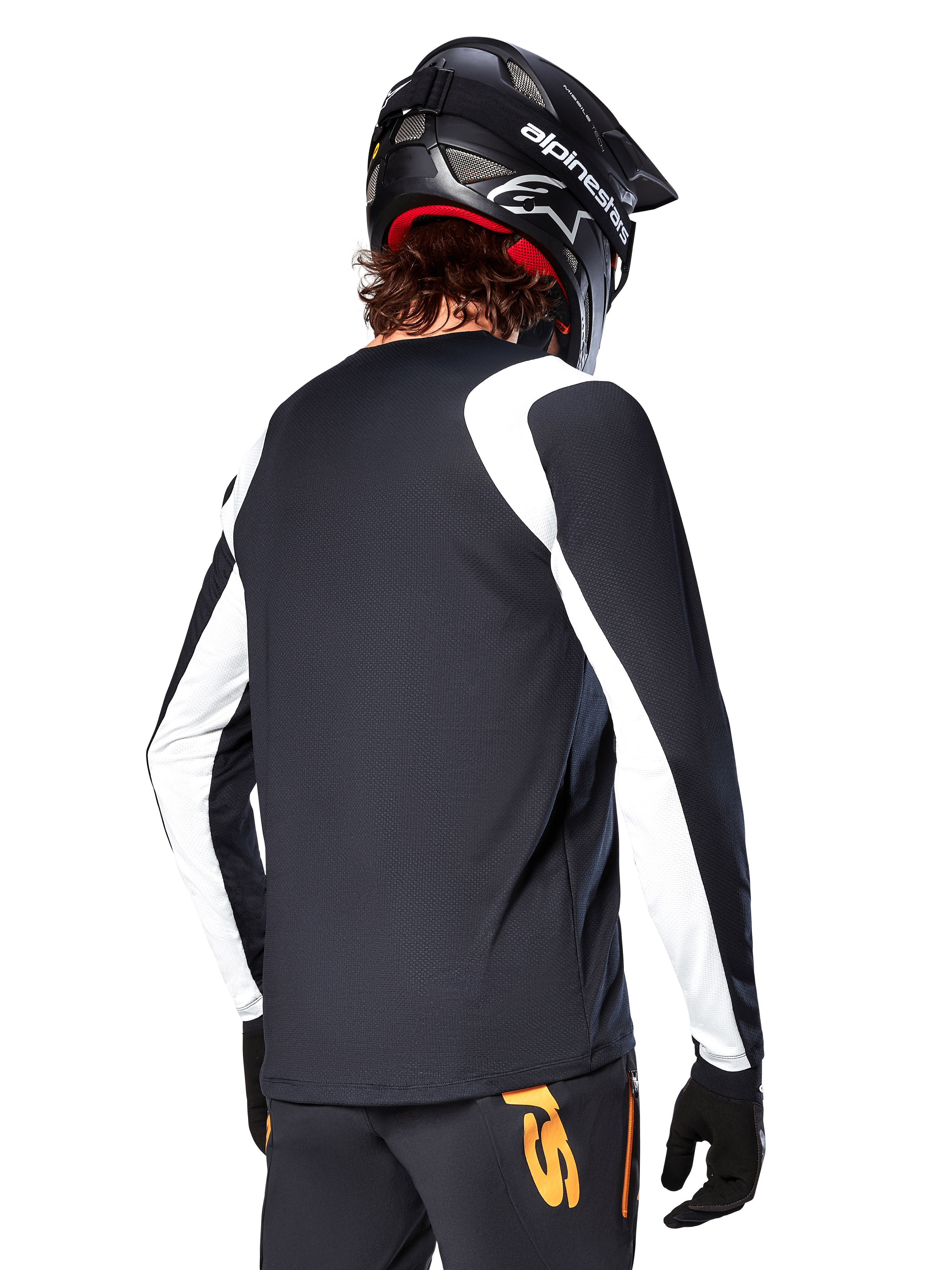 MTB-rijder draagt Alpinestars A-Supra Oscar jersey met lange mouwen, zwart met witte panelen op de schouders en mouwen, van achteren gezien, zwarte helm en handschoenen, broek met oranje accenten, duurzame off-road fietskleding