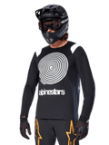 Alpinestars A-Supra Oscar Jersey met lange mouwen, MTB-fietsshirt, zwart en wit, voorzien van een opvallend wit spiraalontwerp en Alpinestars-logo op de borst, gedragen met een zwarte full-face helm en bril, prestatiegerichte mountainbikekleding