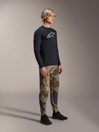 Alpinestars A-Dura Camo broek, MTB-broek, bruine camouflage, gedragen met een zwart A-Dura Astar jersey met lange mouwen en zwarte schoenen, technische mountainbikekleding voor trailrijden