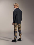 Alpinestars A-Dura Camo broek, MTB-broek, bruine camouflage, gedragen met een zwart jersey met lange mouwen en zwarte sneakers, achteraanzicht met toelopende pijpen en elastische manchetten, prestatiegerichte kleding voor off-road fietsen
