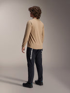Alpinestars A-Dura Astar Long Sleeve Jersey in lichtbruin, achteraanzicht van een mannelijk model toont het drop tail-ontwerp, gecombineerd met zwarte broek en schoenen, casual mountainbike-prestatiekleding