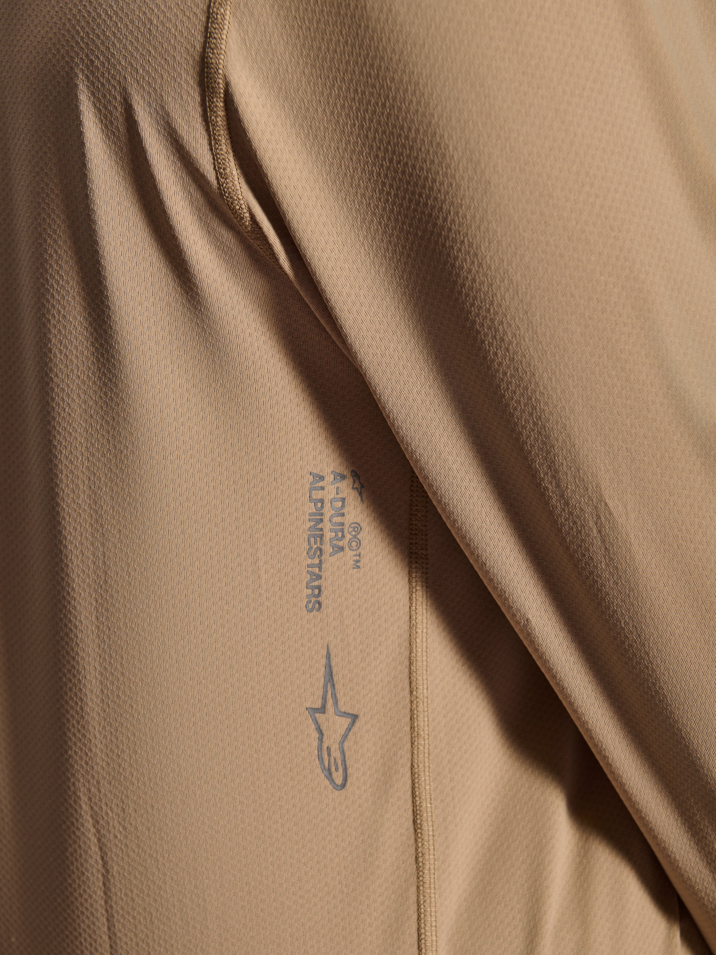 Alpinestars A-Dura Astar Jersey met lange mouwen, MTB-fietsshirt, bruin, close-up met jacquard stoftextuur, geprint Astars-logo en A-Dura-woordmerk, technische mountainbikekleding