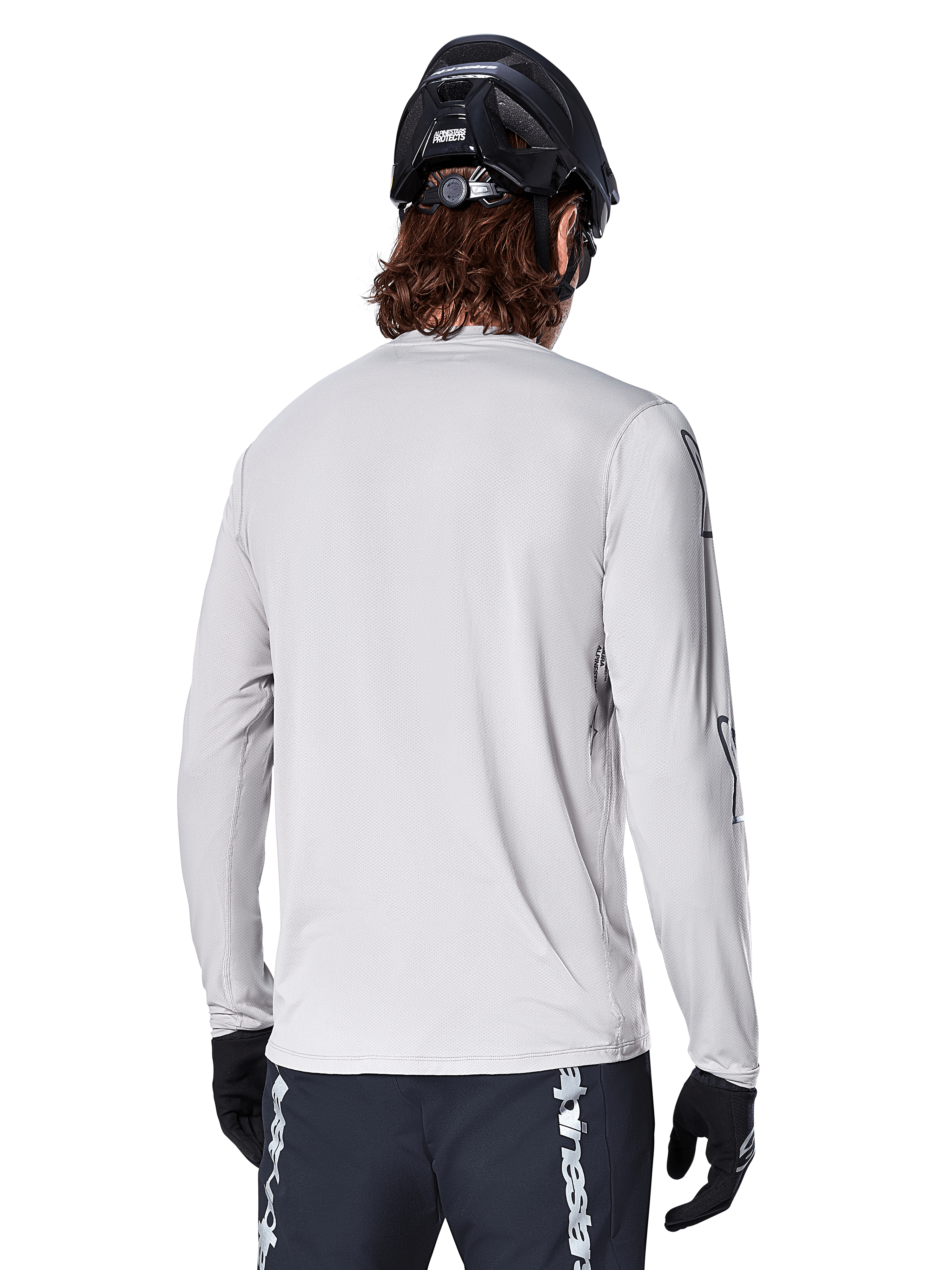 Alpinestars A-Dura Switch Long Sleeve Jersey, Light Gray, back view of a mountain biker wearing a black MTB helmet and gloves, featuring a drop tail for extra coverage and textured jacquard fabric, performance cycling gear.
