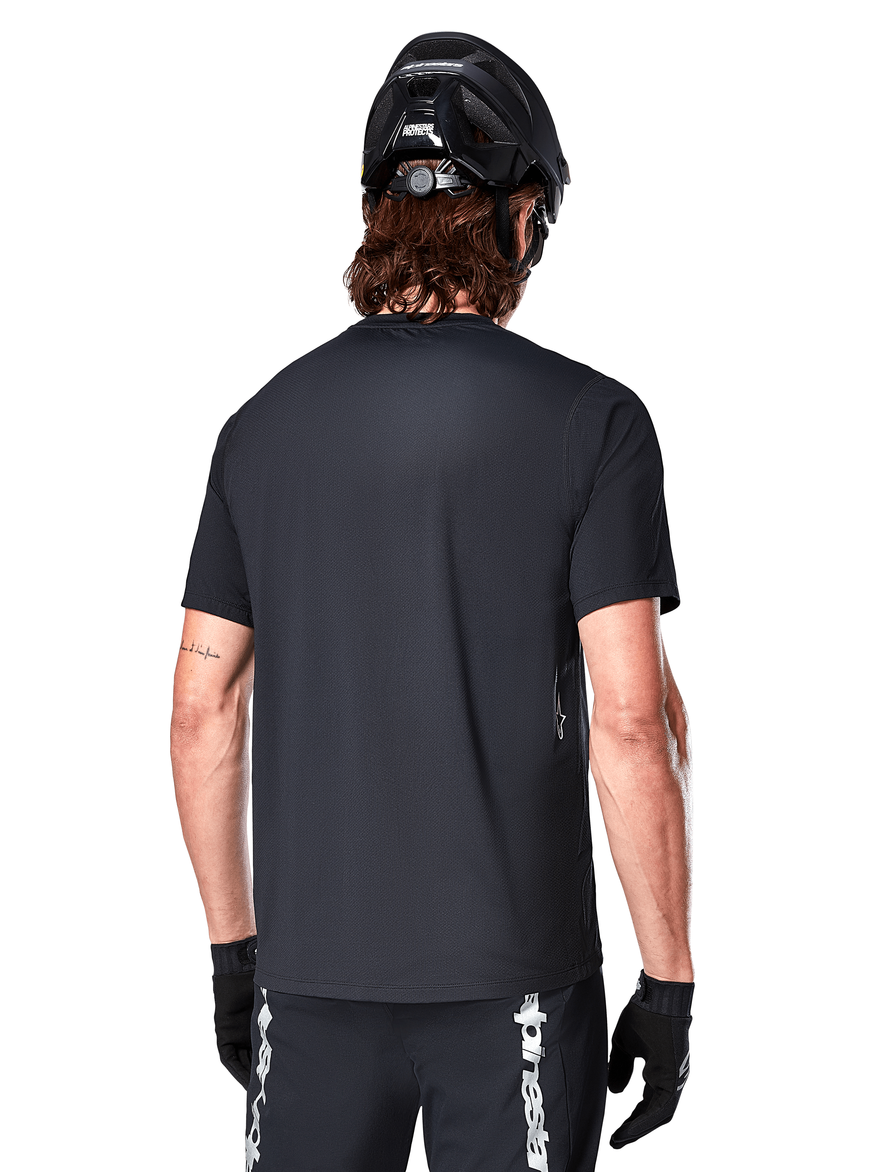 Alpinestars A-Dura Switch Short Sleeve Jersey, Black, rear view on a model wearing a black cycling helmet and MTB shorts, highlighting the regular fit and longer drop tail designed for mountain biking.