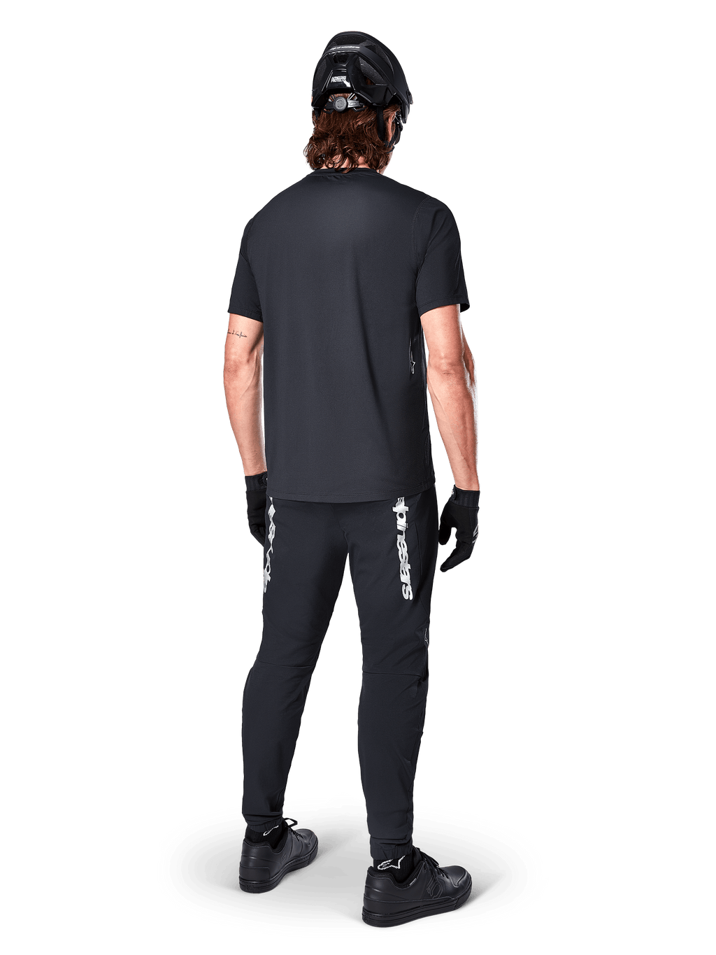 Alpinestars A-Dura Switch Jersey - Short Sleeve, Black, back view of rider wearing complete mountain bike gear, including matching black pants with white wordmark branding, black helmet, and gloves, performance cycling apparel for trail riding