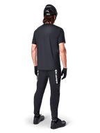 Alpinestars A-Dura Switch Jersey - Short Sleeve, Black, back view of rider wearing complete mountain bike gear, including matching black pants with white wordmark branding, black helmet, and gloves, performance cycling apparel for trail riding