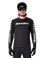Mannelijke rijder in Alpinestars A-Dura Dri Oscar Jersey met lange mouwen, zwart reflecterend, voorzien van een wit Alpinestars-woordmerk op de borst en zilveren reflecterende graphics op de mouwen, gecombineerd met een zwarte MTB-helm, zonnebril en zwarte handschoenen, performance fietskleding
