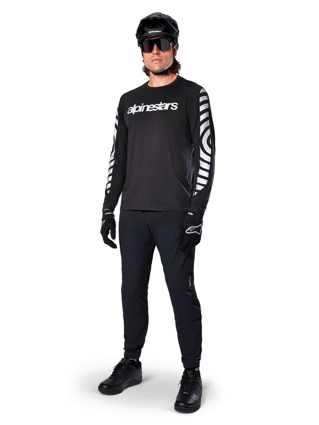 Alpinestars A-Dura Dri Oscar Jersey met lange mouwen, Black Reflective, met opvallend wit Alpinestars-woordmerk op de borst en reflecterende grafische patronen op de mouwen, gedragen met zwarte mountainbikebroek, helm en handschoenen, technische MTB-kleding