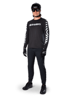 Alpinestars A-Dura Dri Oscar Jersey met lange mouwen, Black Reflective, met opvallend wit Alpinestars-woordmerk op de borst en reflecterende grafische patronen op de mouwen, gedragen met zwarte mountainbikebroek, helm en handschoenen, technische MTB-kleding
