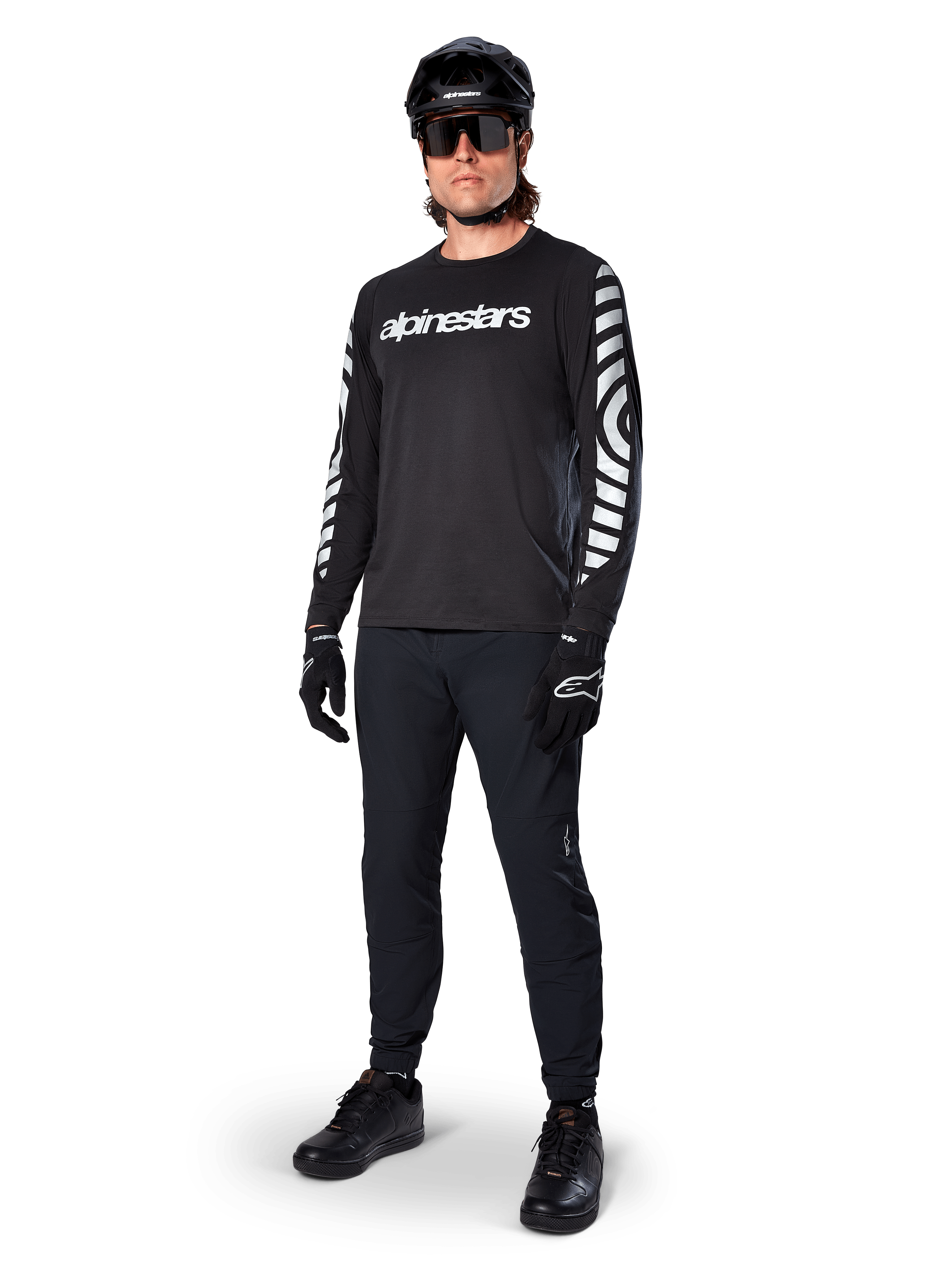 Alpinestars A-Dura Dri Oscar Jersey met lange mouwen, Black Reflective, met opvallend wit Alpinestars-woordmerk op de borst en reflecterende grafische patronen op de mouwen, gedragen met zwarte mountainbikebroek, helm en handschoenen, technische MTB-kleding