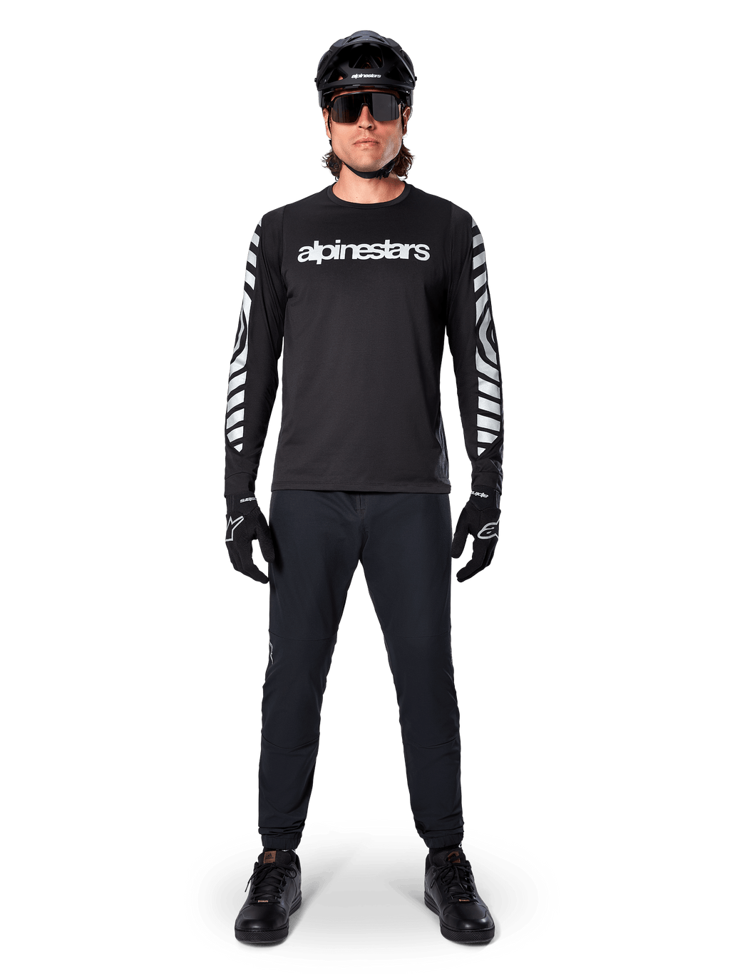 Alpinestars A-Dura Dri Oscar Jersey met lange mouwen in Black Reflective, gedragen met een zwarte helm en zonnebril, voorzien van een wit logo op de borst en reflecterende grafische patronen op de mouwen, MTB-kleding voor off-road rijden
