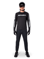Alpinestars A-Dura Dri Oscar Jersey met lange mouwen in Black Reflective, gedragen met een zwarte helm en zonnebril, voorzien van een wit logo op de borst en reflecterende grafische patronen op de mouwen, MTB-kleding voor off-road rijden