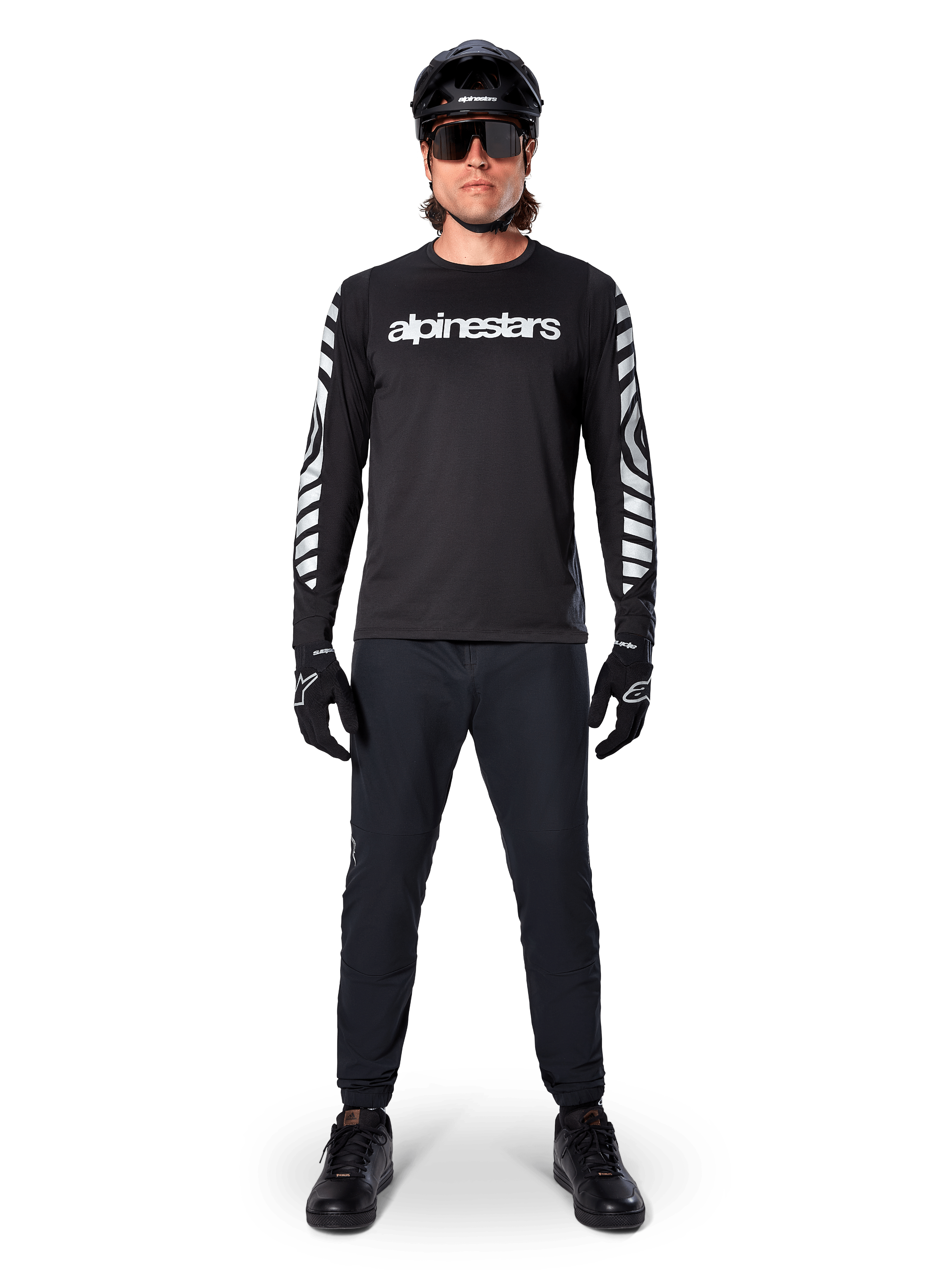 Alpinestars A-Dura Dri Oscar Jersey met lange mouwen in Black Reflective, gedragen met een zwarte helm en zonnebril, voorzien van een wit logo op de borst en reflecterende grafische patronen op de mouwen, MTB-kleding voor off-road rijden