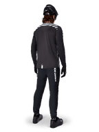 Mountainbiker die de Alpinestars A-Dura Dri Oscar Jersey met lange mouwen in Black Reflective draagt, van achteren gezien, gecombineerd met een zwarte technische broek, helm en handschoenen, voorzien van reflecterende streepgraphics op de schouders en een langere achterzijde voor off-road fietsen.