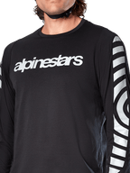 Alpinestars A-Dura Dri Oscar jersey met lange mouwen, Black Reflective, close-up met wit Alpinestars-logo op de borst en reflecterende cirkelvormige graphics op de mouwen, technische fietskleding voor mountainbiken