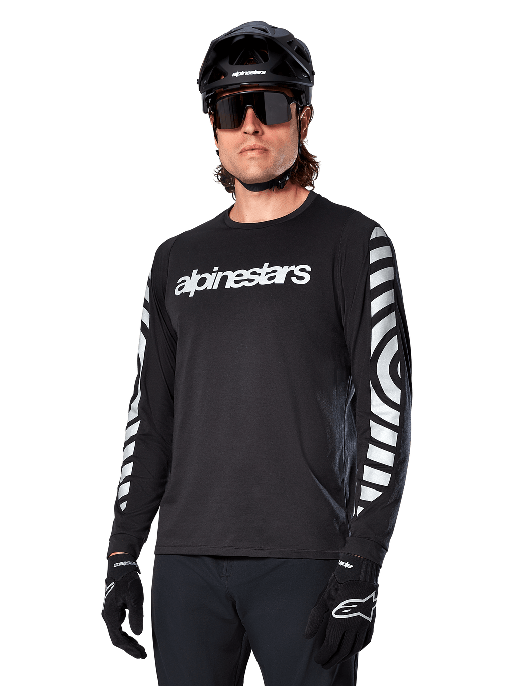 Alpinestars A-Dura Dri Oscar fietsshirt met lange mouwen, MTB-fietsshirt, zwart reflecterend, met een wit woordmerk op de borst en opvallende reflecterende cirkelvormige graphics op de mouwen, gedragen met een zwarte helm en zonnebril, technische vochtafvoerende kleding voor off-road mountainbiken
