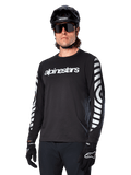Alpinestars A-Dura Dri Oscar fietsshirt met lange mouwen, MTB-fietsshirt, zwart reflecterend, met een wit woordmerk op de borst en opvallende reflecterende cirkelvormige graphics op de mouwen, gedragen met een zwarte helm en zonnebril, technische vochtafvoerende kleding voor off-road mountainbiken