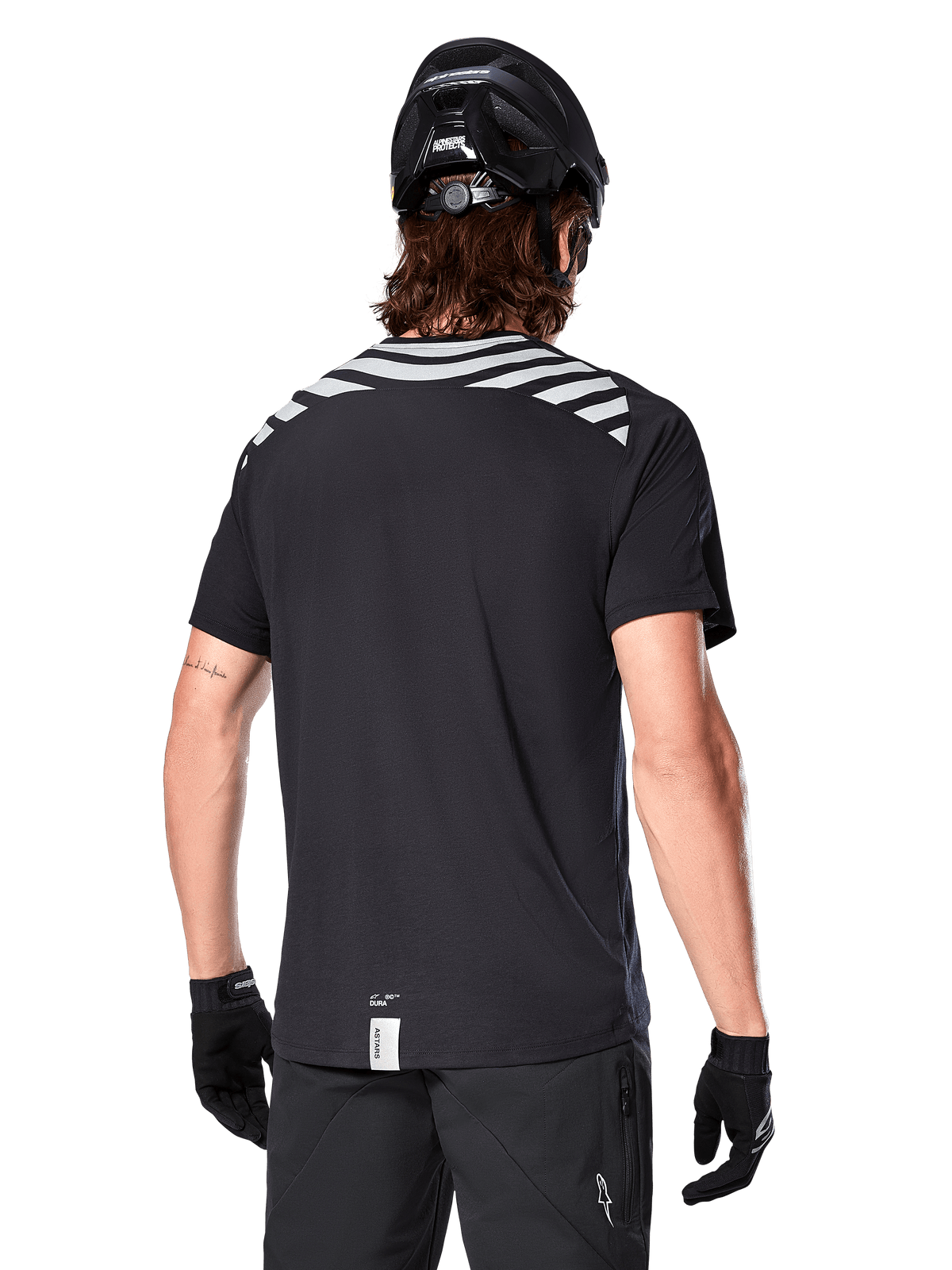 Alpinestars A-Dura Dri Oscar Jersey, MTB-jersey met korte mouwen, Black Reflective, achteraanzicht op model met fietshelm en handschoenen, met reflecterende grijze schouderstrepen en een verlengd achterpand, vochtafvoerende technische stof voor mountainbiken