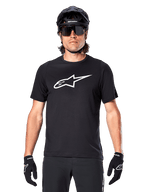 Alpinestars A-Dura Dri Oscar Jersey met korte mouwen, Black Reflective, gedragen met zwarte MTB-helm, zonnebril en handschoenen, voorzien van een opvallend wit logo op de borst, technische kleding voor mountainbiken