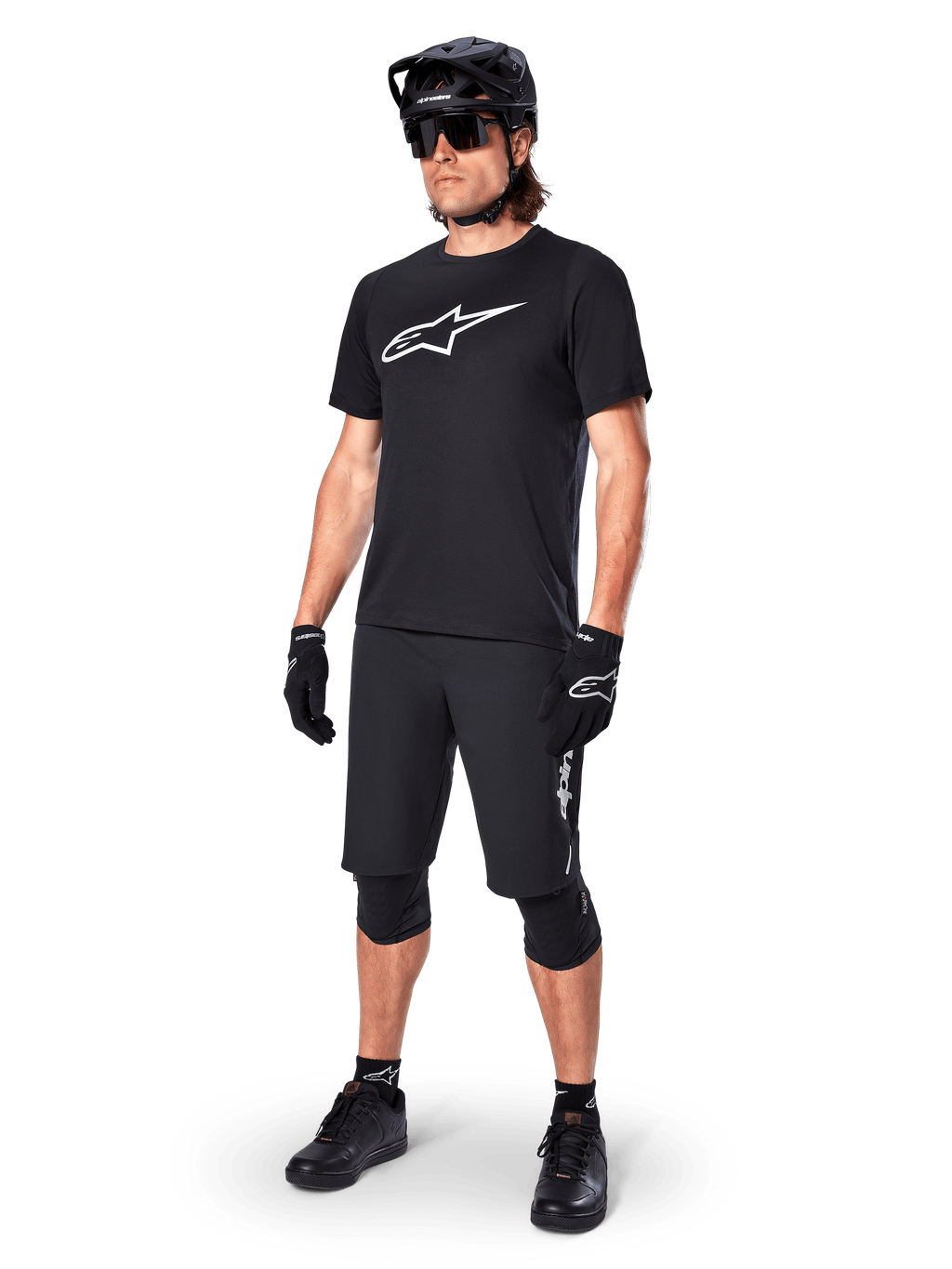 Mountainbiker draagt het Alpinestars A-Dura Dri Oscar fietsshirt met korte mouwen in Black Reflective, voorzien van een groot wit logo op de borst, gecombineerd met bijpassende zwarte MTB-short, handschoenen en helm, technische fietskleding voor off-road prestaties