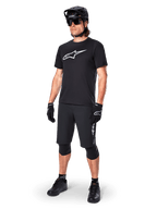 Mountainbiker draagt het Alpinestars A-Dura Dri Oscar fietsshirt met korte mouwen in Black Reflective, voorzien van een groot wit logo op de borst, gecombineerd met bijpassende zwarte MTB-short, handschoenen en helm, technische fietskleding voor off-road prestaties