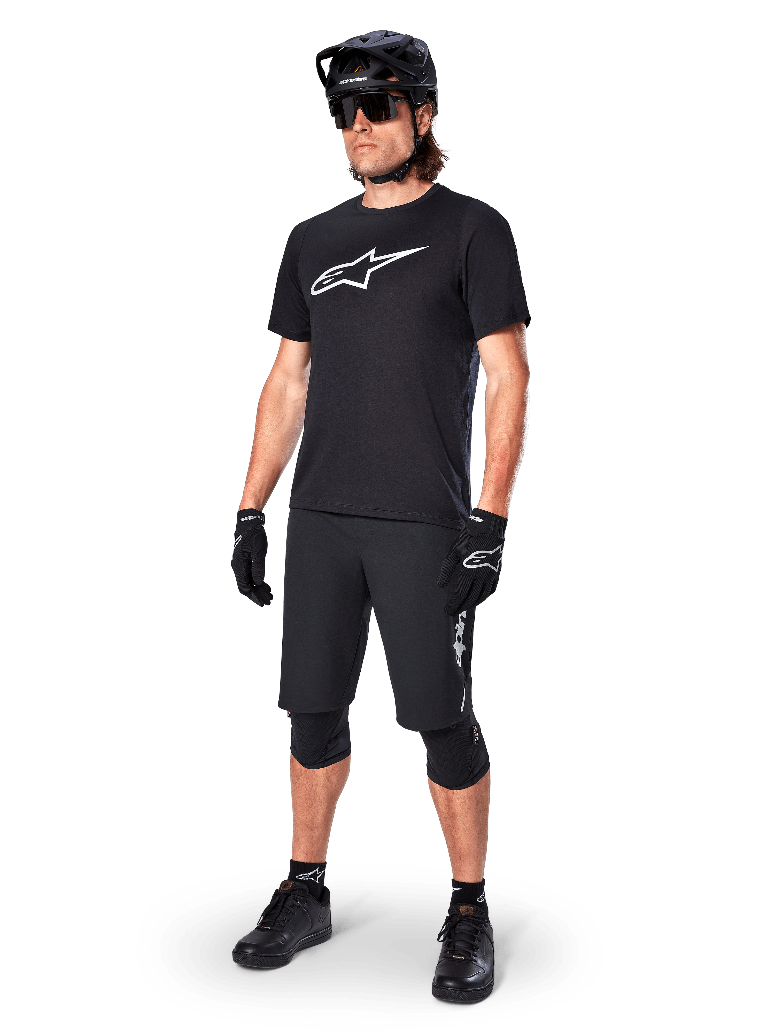 Mountainbiker draagt het Alpinestars A-Dura Dri Oscar fietsshirt met korte mouwen in Black Reflective, voorzien van een groot wit logo op de borst, gecombineerd met bijpassende zwarte MTB-short, handschoenen en helm, technische fietskleding voor off-road prestaties