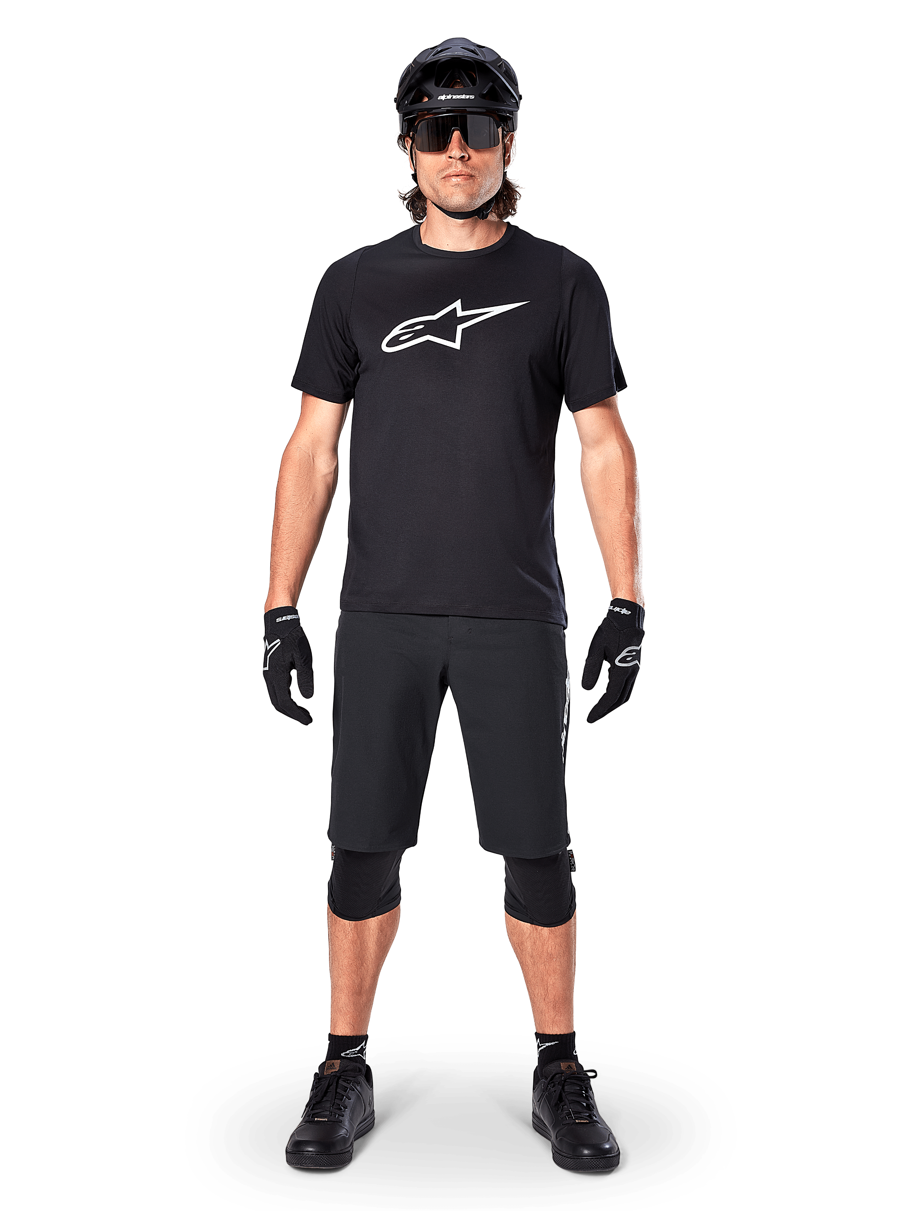 Alpinestars A-Dura Dri Oscar jersey met korte mouwen, Black Reflective, gedragen met bijpassende zwarte MTB-short, handschoenen, kniebeschermers en helm, groot wit Alpinestars-logo op de borst, complete mountainbike-outfit