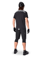 Alpinestars A-Dura Dri Oscar jersey met korte mouwen, Black Reflective, achteraanzicht van een rijder die de jersey draagt met een zwarte mountainbike short, helm en kniebeschermers, voorzien van reflecterende graphics op de schouders en een verlengd achterpand voor MTB-rijden.
