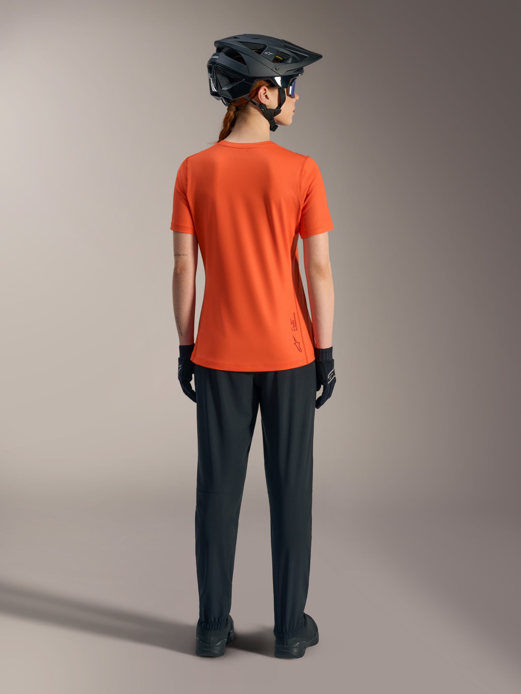 Alpinestars Stella A-Dura Ride fietsshirt voor dames in oranje, achteraanzicht met zwarte MTB-broek en helm.
