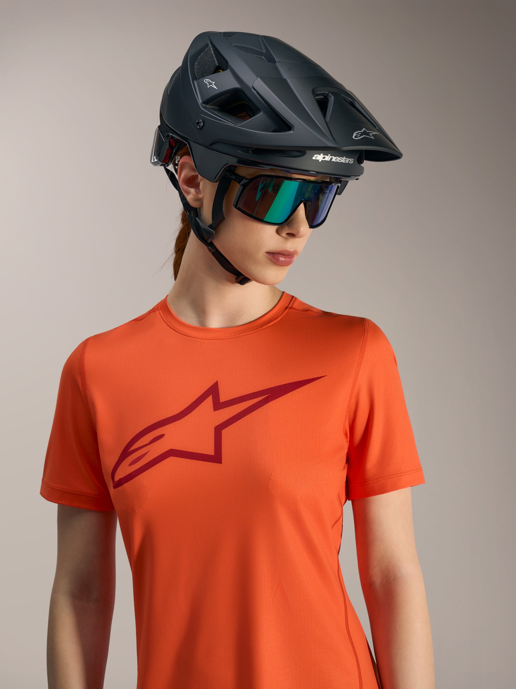 Oranje Stella A-Dura Ride trui met korte mouwen, rood logo, zwarte mountainbikehelm en iriserende zonnebril.