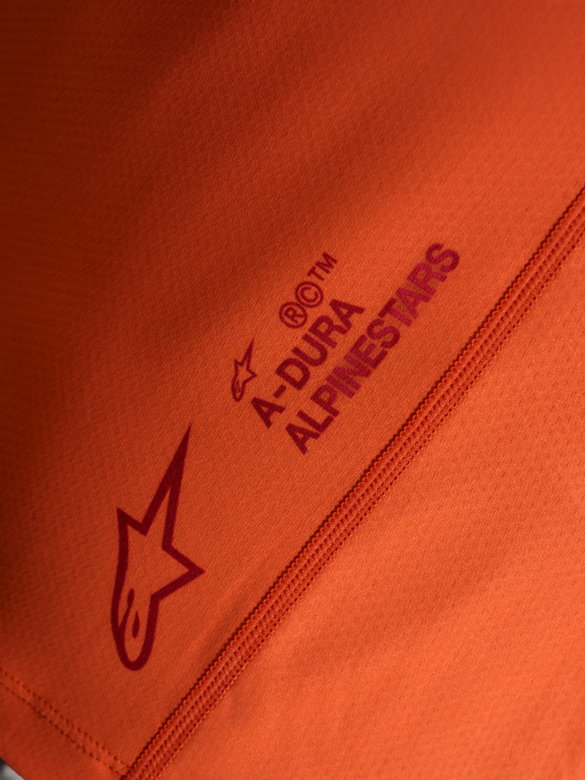 Oranje Stella A-Dura Ride jersey detail met Alpinestars logo en A-DURA woordmerk op technische stretchstof.