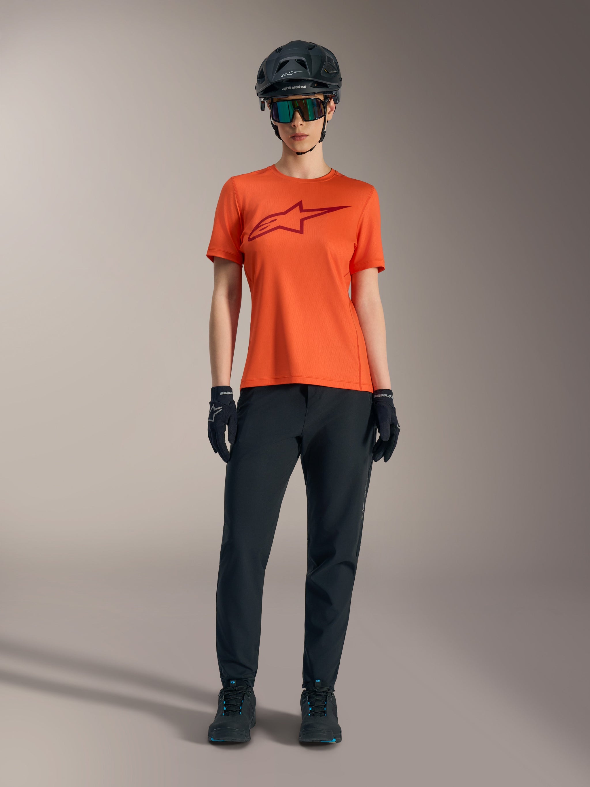 Oranje Stella A-Dura Ride-trui met korte mouwen, bordeauxrood logo, zwarte MTB-uitrusting, helm en handschoenen.