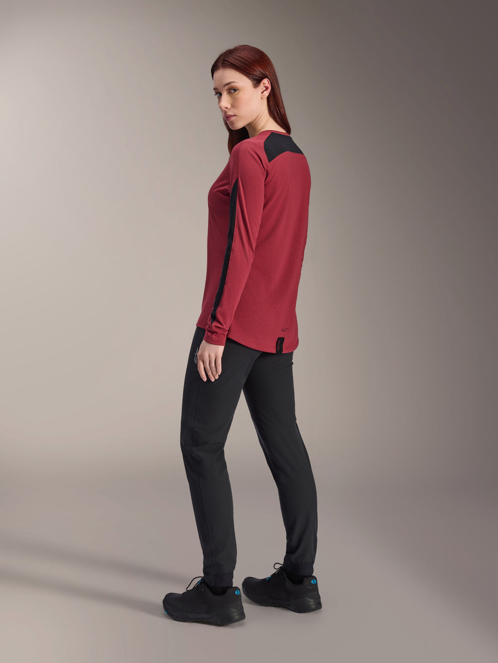 Alpinestars Stella A-Dura Dri Astar damesjersey met lange mouwen, bordeauxrood en zwart, gedragen met zwarte MTB-broek en zwarte schoenen, achteraanzicht in profiel, gerecyclede drirelease®-stof met meshpanelen, technische mountainbikekleding