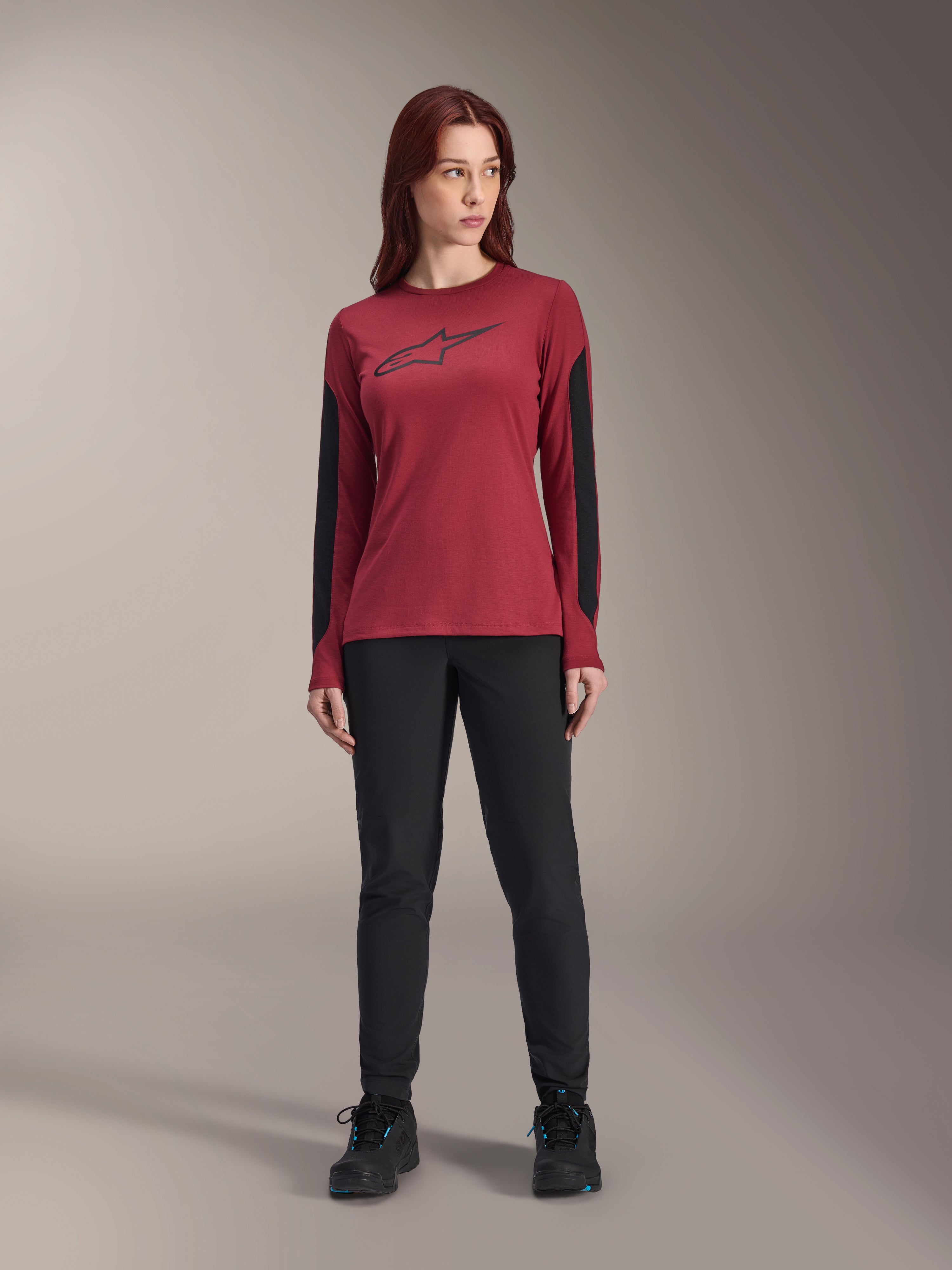 Alpinestars Stella A-Dura Dri Astar fietsshirt met lange mouwen voor dames in bordeauxrood, met een zwart Astars-logo op de borst en zwarte mesh-panelen op de mouwen, gestyled met een zwarte technische broek en sportschoenen, hoogwaardige mountainbikekleding voor dames.