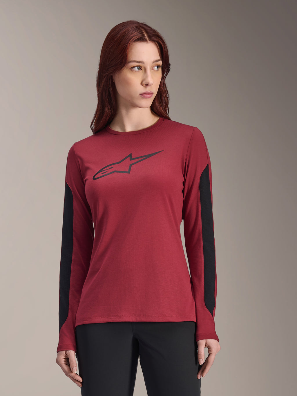 Alpinestars Stella A-Dura Dri Astar fietsshirt voor dames, lange mouwen, bordeauxrood met zwarte zijpanelen, zwart logo op de borst, vochtafvoerende MTB-kleding, specifieke damespasvorm, vrouw draagt shirt met zwarte broek