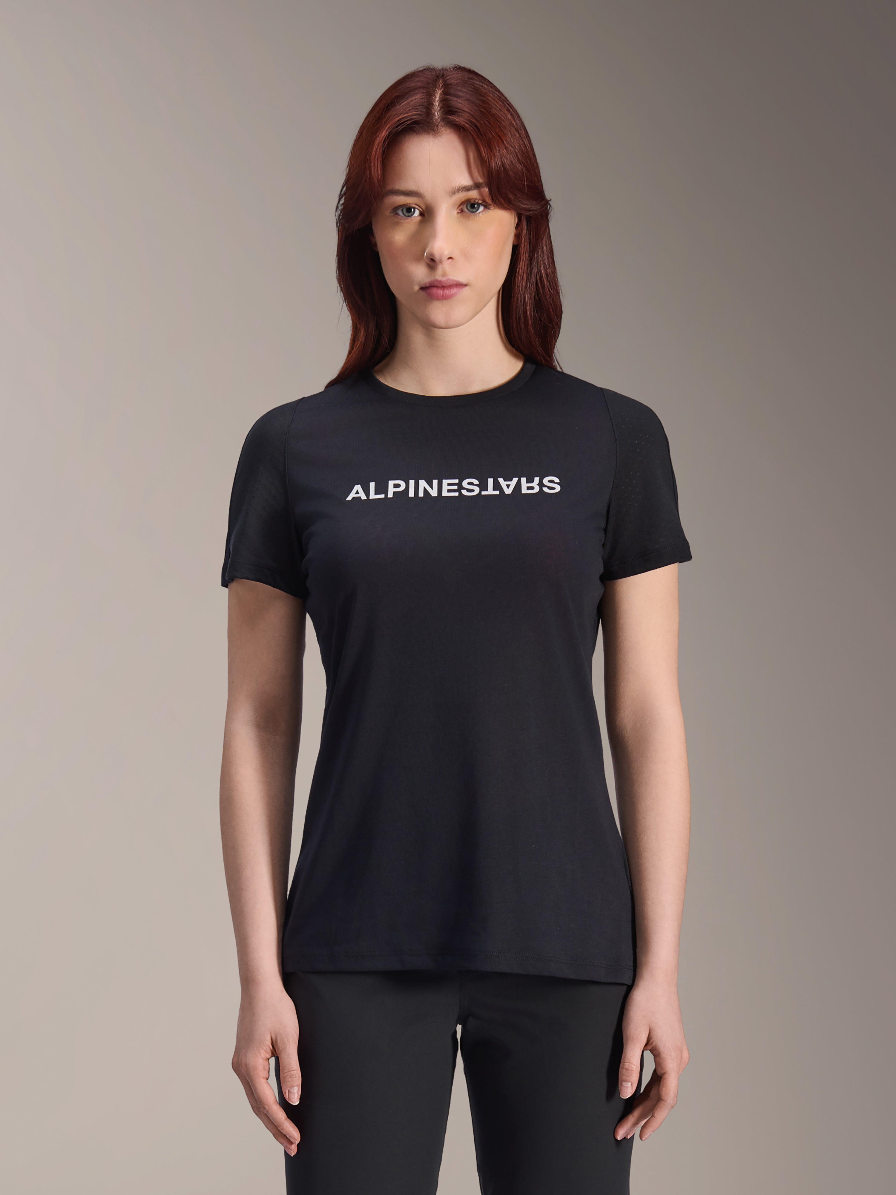Alpinestars Stella A-Dura Dri Switch Jersey, MTB-shirt met korte mouwen voor dames, zwart met wit Alpinestars-logo op de borst, casual performance pasvorm, technische vochtafvoerende stof voor mountainbiken, vrouw met rood haar draagt het shirt