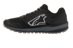 Alpinestars Meta Trail schoenen, performance hardloopschoen, zwart en donkergrijs, zijprofiel met groot wit Astars-logo, donkergrijze tussenzool, oliebestendige rubberen profielzool, ontworpen voor paddockcomfort en gebruik door motorsportteams.