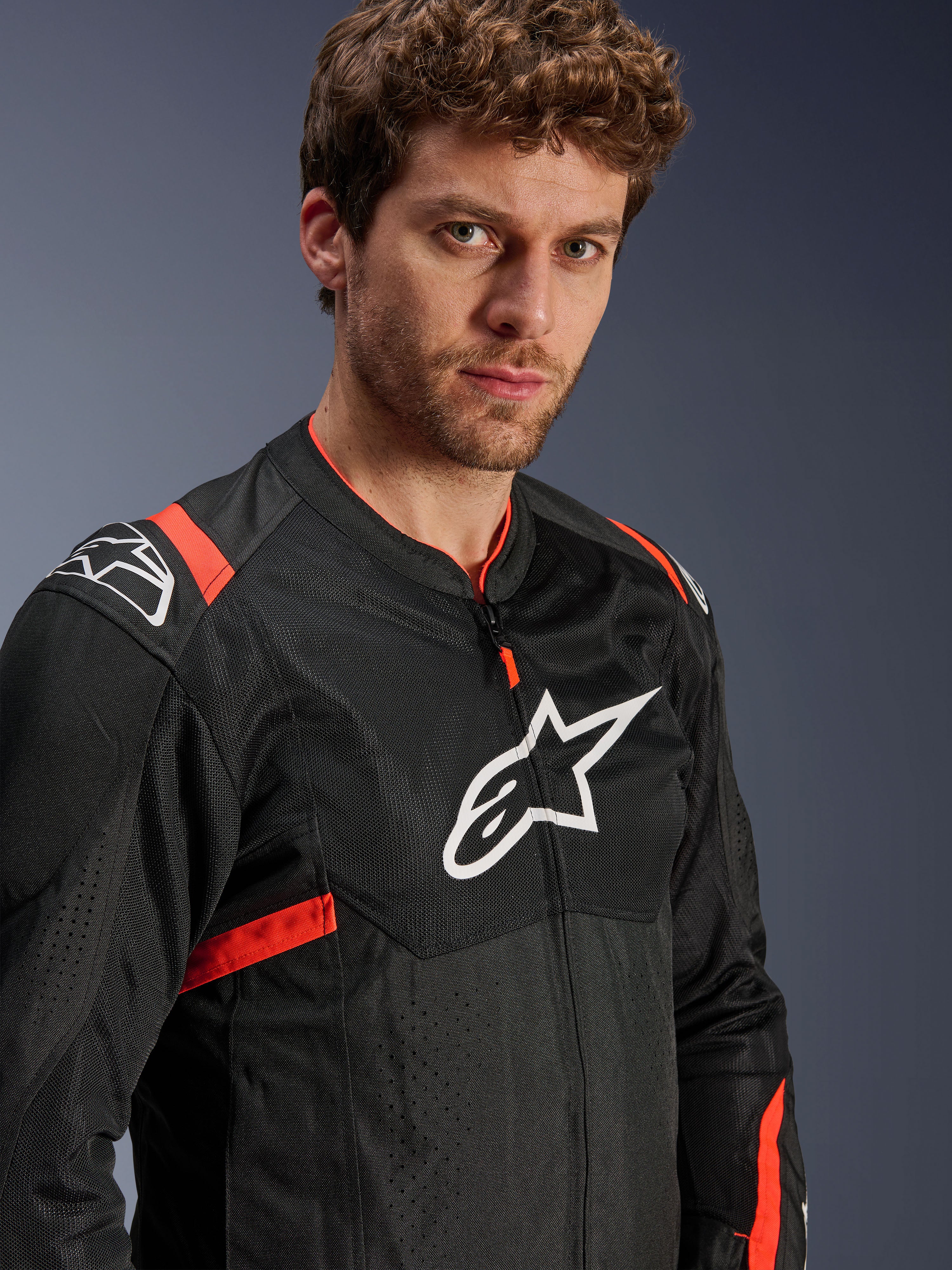 Alpinestars T-Sps Air V2 Jas, zwart met Red Fluo accenten, textiel mesh motorjas, gedragen door model, voorzien van wit Alpinestars-logo op de borst en schouders, ademende mesh-panelen, sportieve stedelijke rijstijl
