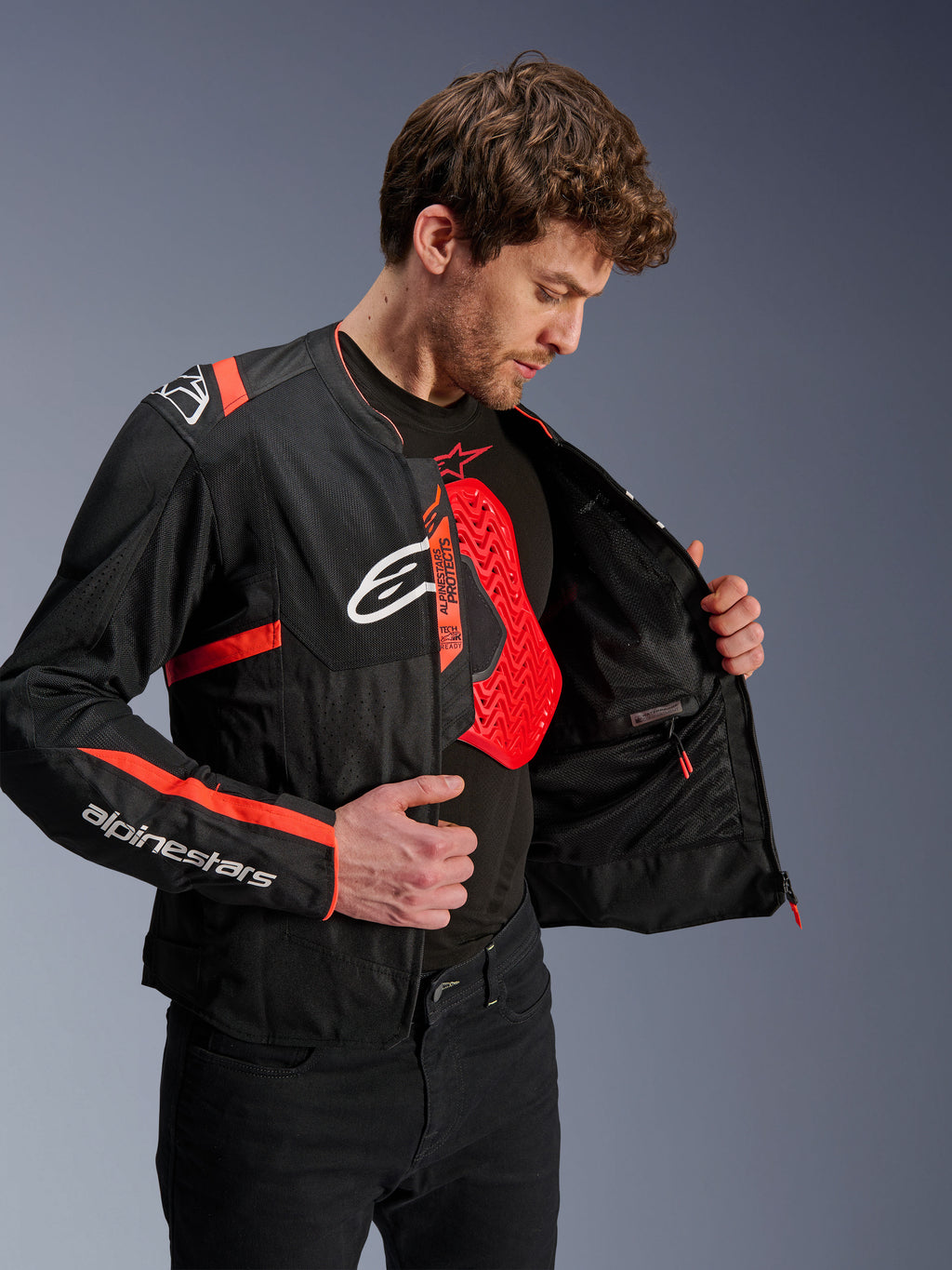 Alpinestars T-Sps Air V2 Jas in Black and Red Fluo, gedragen door een model die de mesh-voering aan de binnenzijde en een rode Nucleon borstbeschermer toont, voorzien van witte Alpinestars-logo's en tech mesh-panelen
