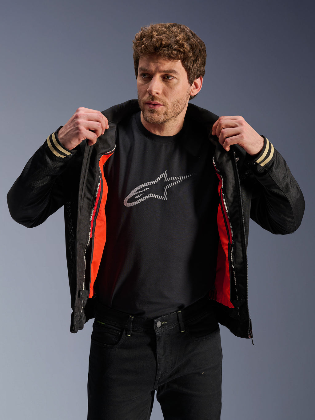 Man die de Alpinestars Ignite Air Jas draagt, zwart, voorzien van een mesh body en feloranje uitneembare winddichte voering, gecombineerd met een zwart t-shirt met Astars-logo en een zwarte broek, urban contemporary motorstijl