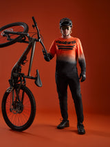 Oranje-zwart A-Dura ASTARS Jersey 2.0 met kleurverloop en logo, gedragen met volledige mountainbike-uitrusting.
