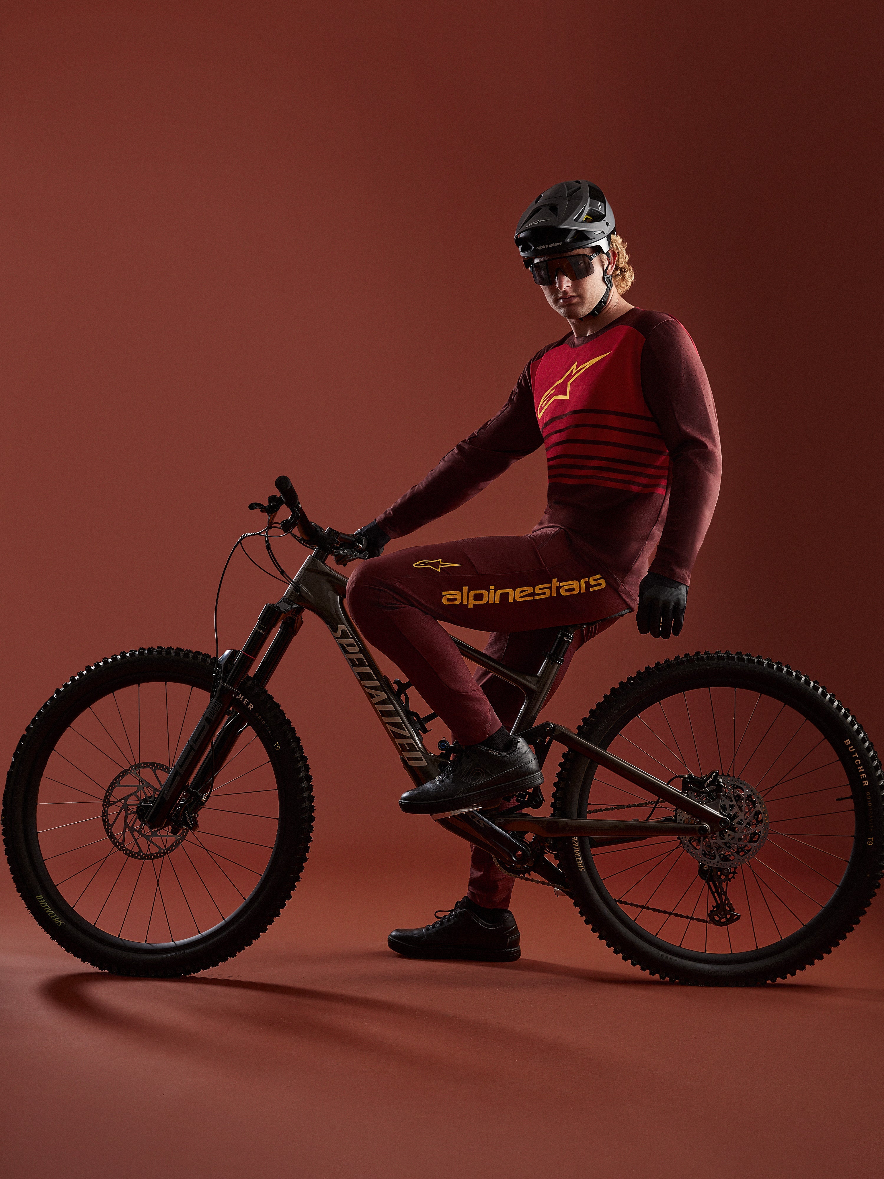 Mountainbiker in Bordeaux A-Dura Elite Jersey 2.0 en bijpassende broek op een Specialized mountainbike in een studio.