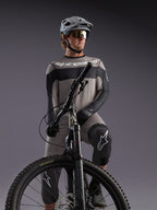 Grijze Alpinestars A-Dura Race jersey met lange mouwen op een MTB-rijder, met zwarte accenten en professionele gear.