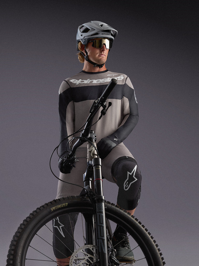 Grijze Alpinestars A-Dura Race jersey met lange mouwen op een MTB-rijder, met zwarte accenten en professionele gear.