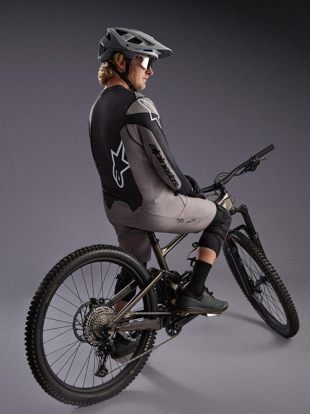 Grijze A-Dura Race trui met lange mouwen op een mountainbiker, met opvallende Alpinestars-logo's en stretchstof.
